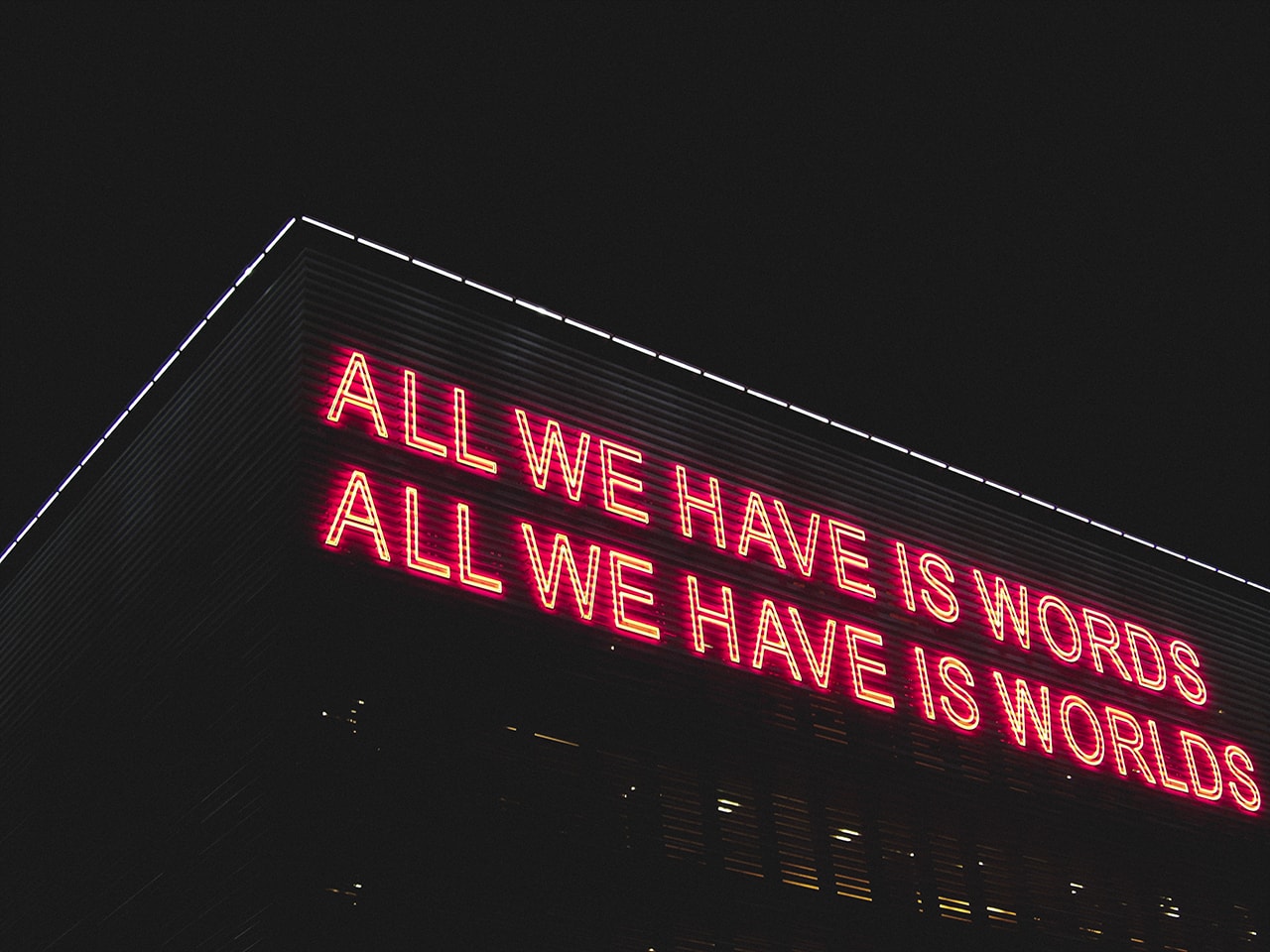 Building with a neon sign saying all we have is words all we have is worlds
