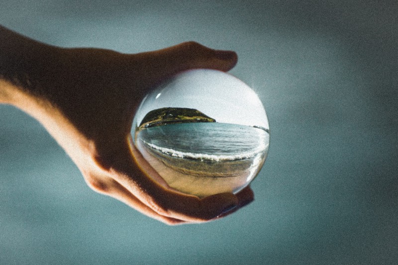 Person holding a see-through glass ball showing the reflection of a beach view