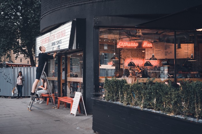 Person installing a name board outside a coffee place | Photo by Toa Heftiba on Unsplash