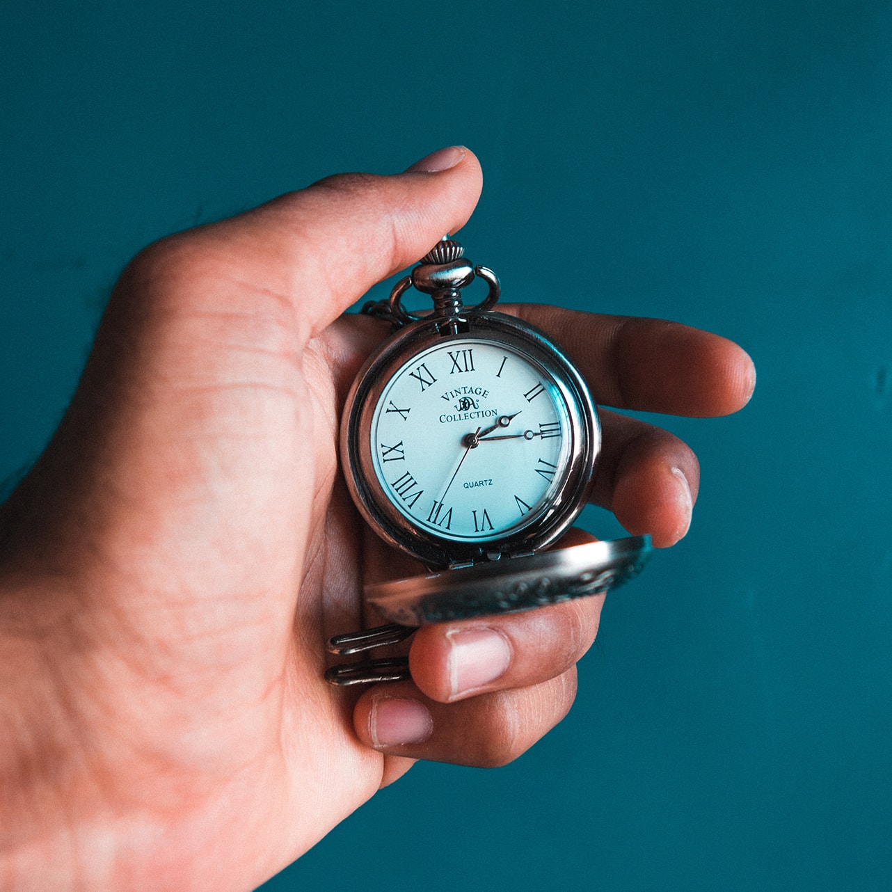 Close-up picture of a pocket watch held in front of a blue background | Photo by Akshar Dave on Unsplash